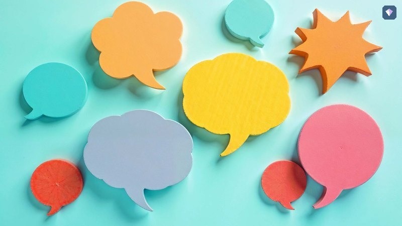 Paper speech bubbles in bright colours laid out on a turquoise background