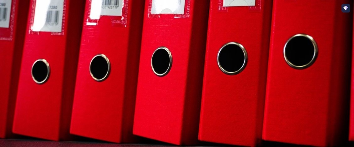 A shelf of red ring binders standing side by side