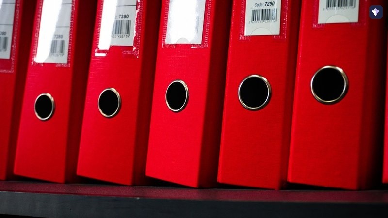 A shelf of red ring binders standing side by side