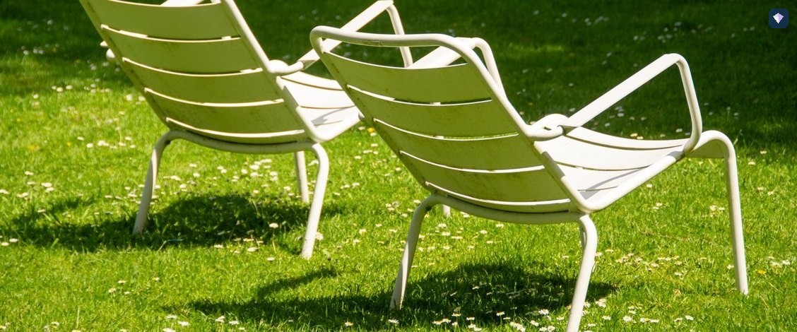 Two white metal chairs standing together on a green lawn