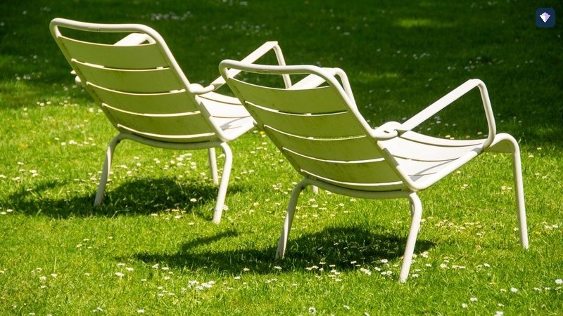 Two white metal chairs standing together on a green lawn