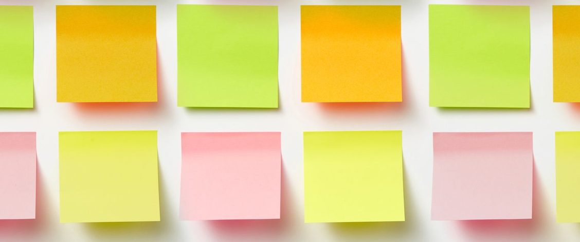 Rows of blank orange, green, yellow and pink sticky notes set out in a grid on a white wall