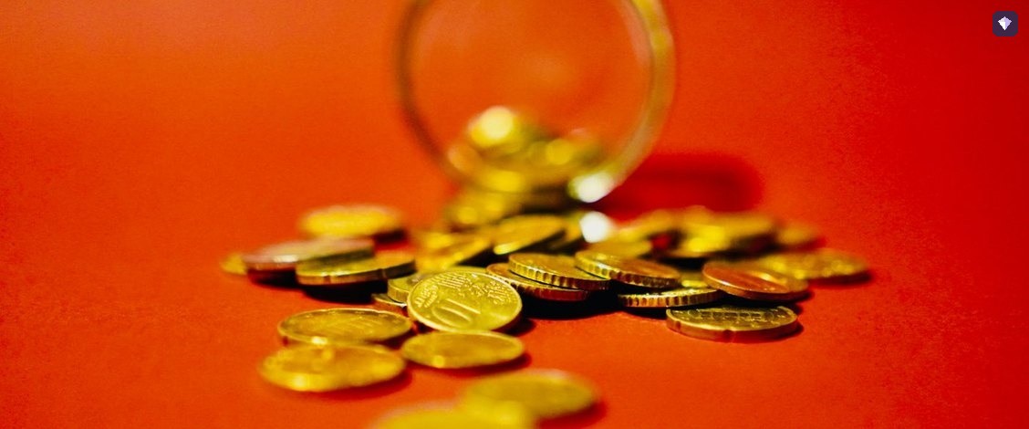 Gold coins spilling from a glass jar onto a red background