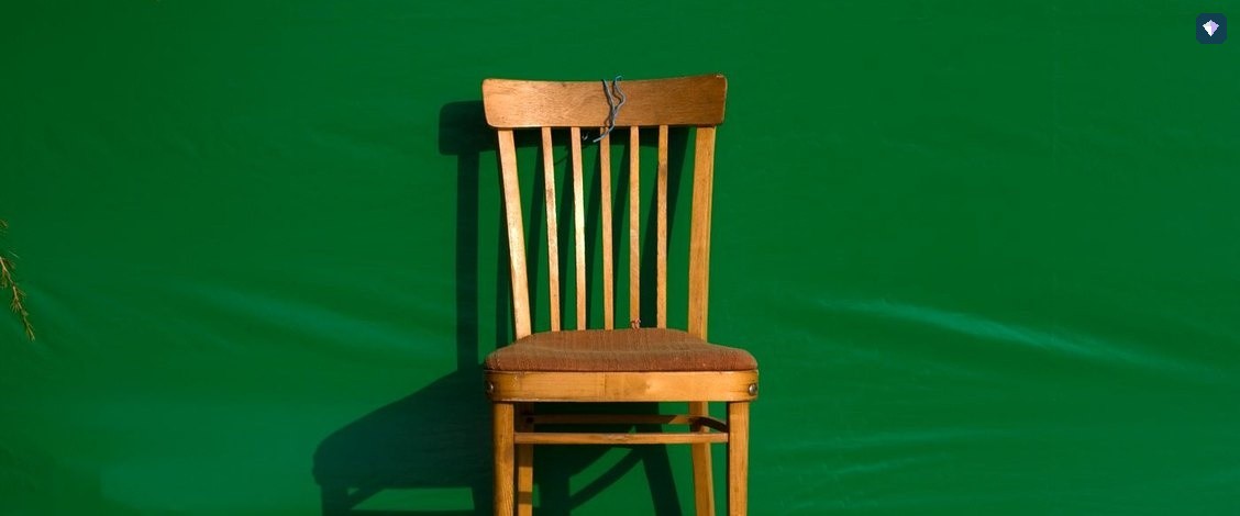 A single wooden chair standing against a vivid green background