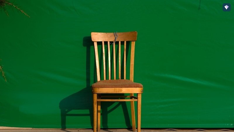 A single wooden chair standing against a vivid green background