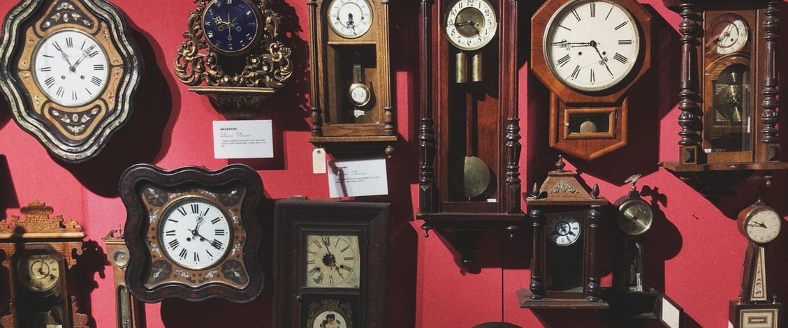 Antique wall clocks of many shapes hanging close together on a red wall