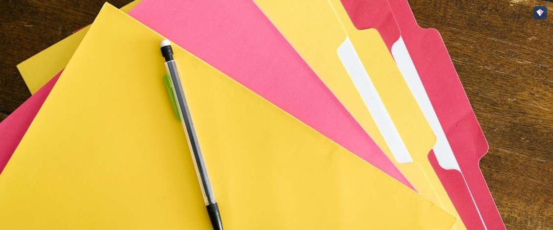 Yellow and pink folders lying closed with a pen across them