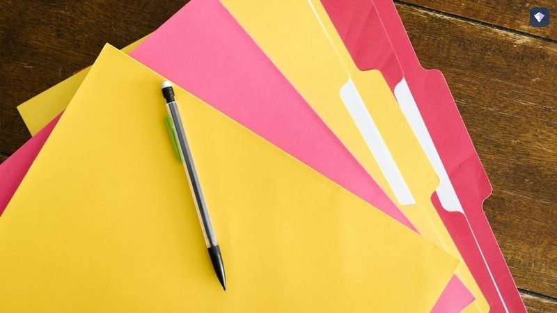 Yellow and pink folders lying closed with a pen across them