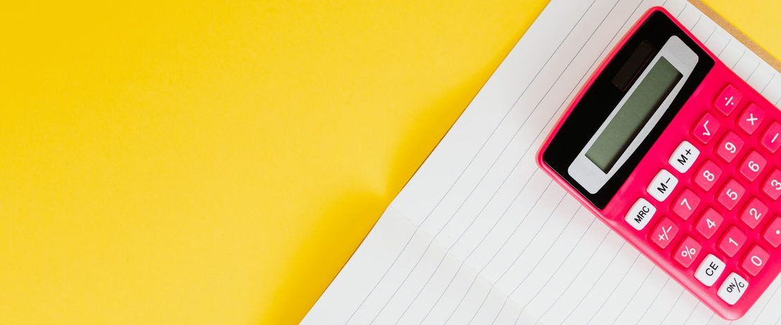 A pink calculator lying on an open lined notebook against a bright yellow background