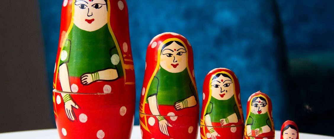 Five red and green painted nesting dolls of the same woman standing in a row from largest to smallest