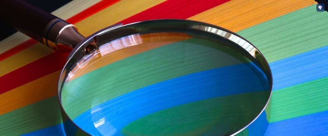 A magnifying glass resting on sheets of rainbow coloured paper