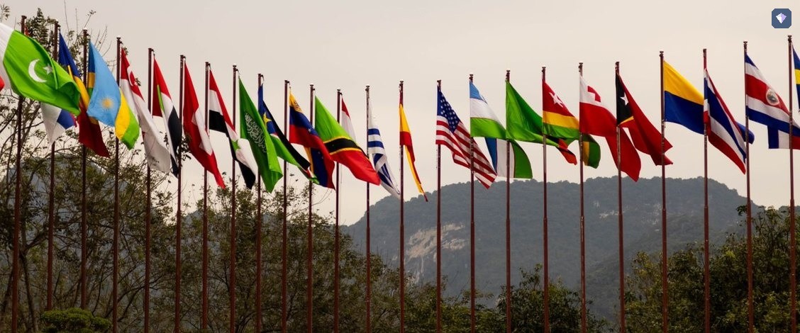 A line of national flags flying from poles in front of hills