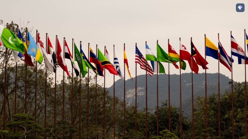 A line of national flags flying from poles in front of hills