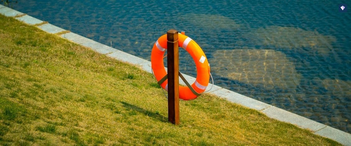 An orange lifebuoy on a post beside open water