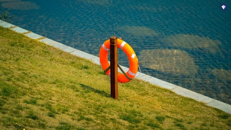 An orange lifebuoy on a post beside open water