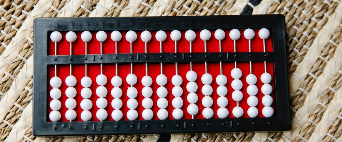 A black abacus with white beads on a red board, lying on a woven straw mat