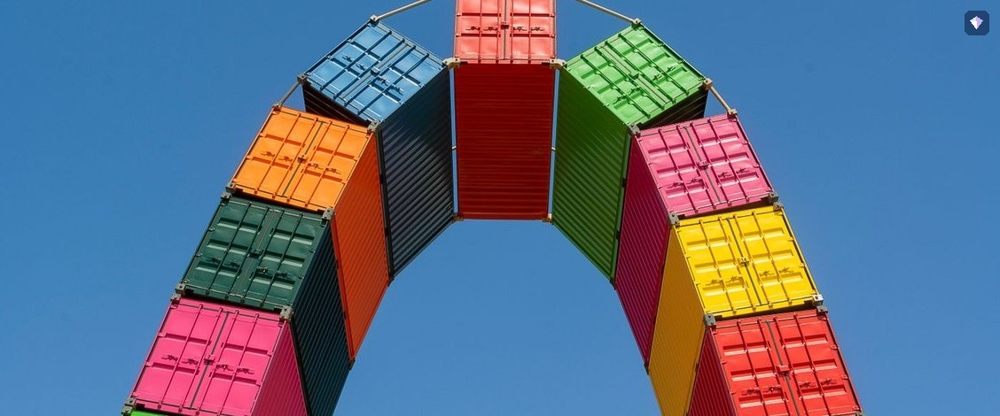 Shipping containers in many colours stacked into an arch against a blue sky