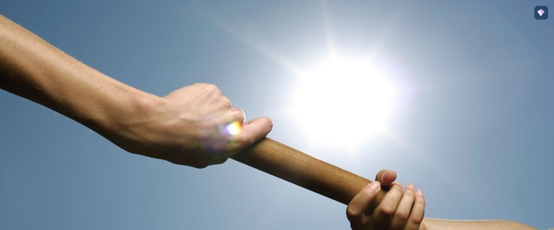 A relay baton passed from one runner's hand to another against a bright sky