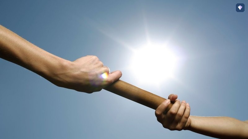 A relay baton passed from one runner's hand to another against a bright sky